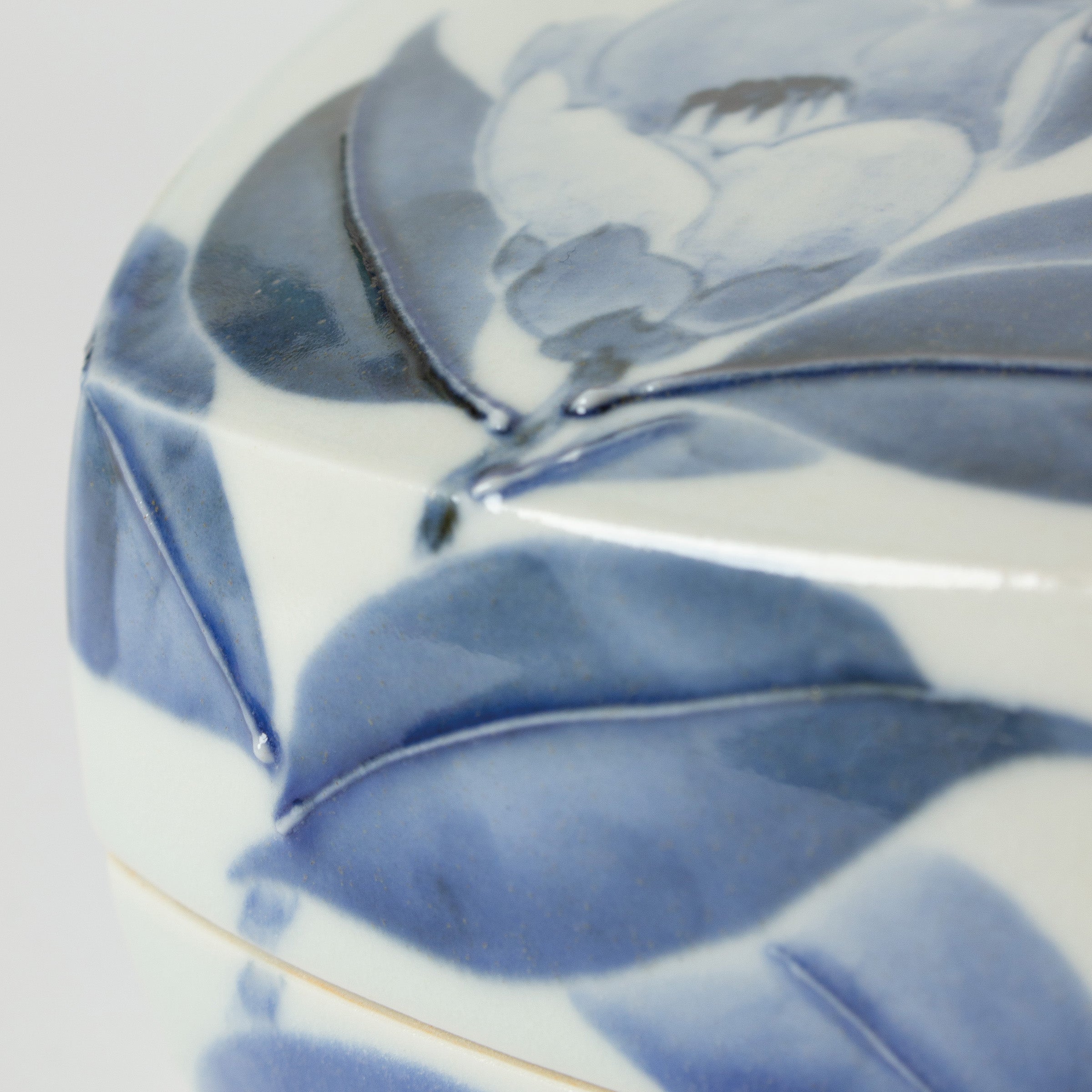 Zoom sur l’émail brillant et les textures de la porcelaine japonaise sur les camélias. Céramique signée Tetsuya Ueda, artisan d’exception.