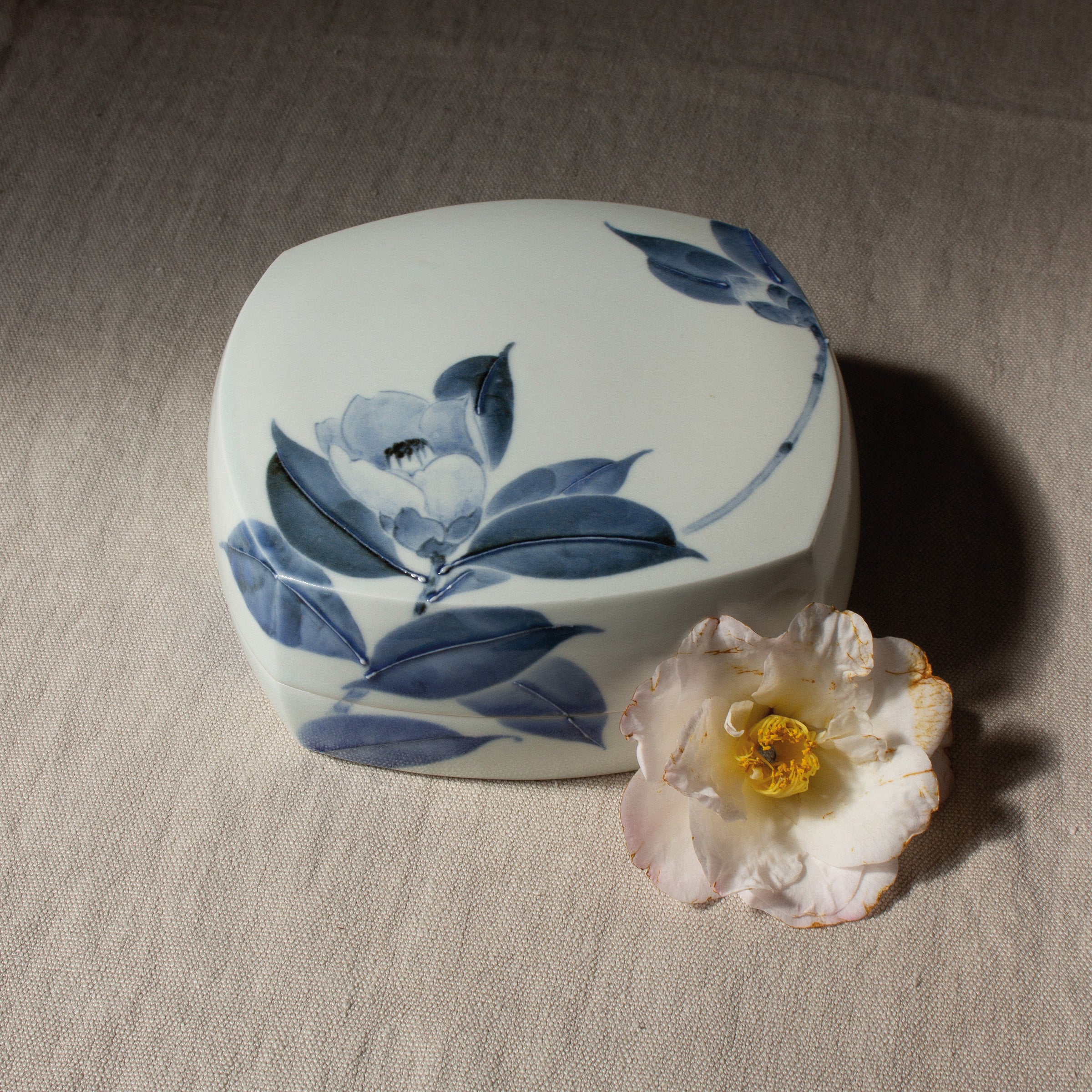 Boîte en porcelaine japonaise de Tetsuya Ueda, vue de face. Motif camélia peint en bleu de cobalt selon la technique du sometsuke. Pièce d’artisanat japonais proposée par Atelier Ikiwa.