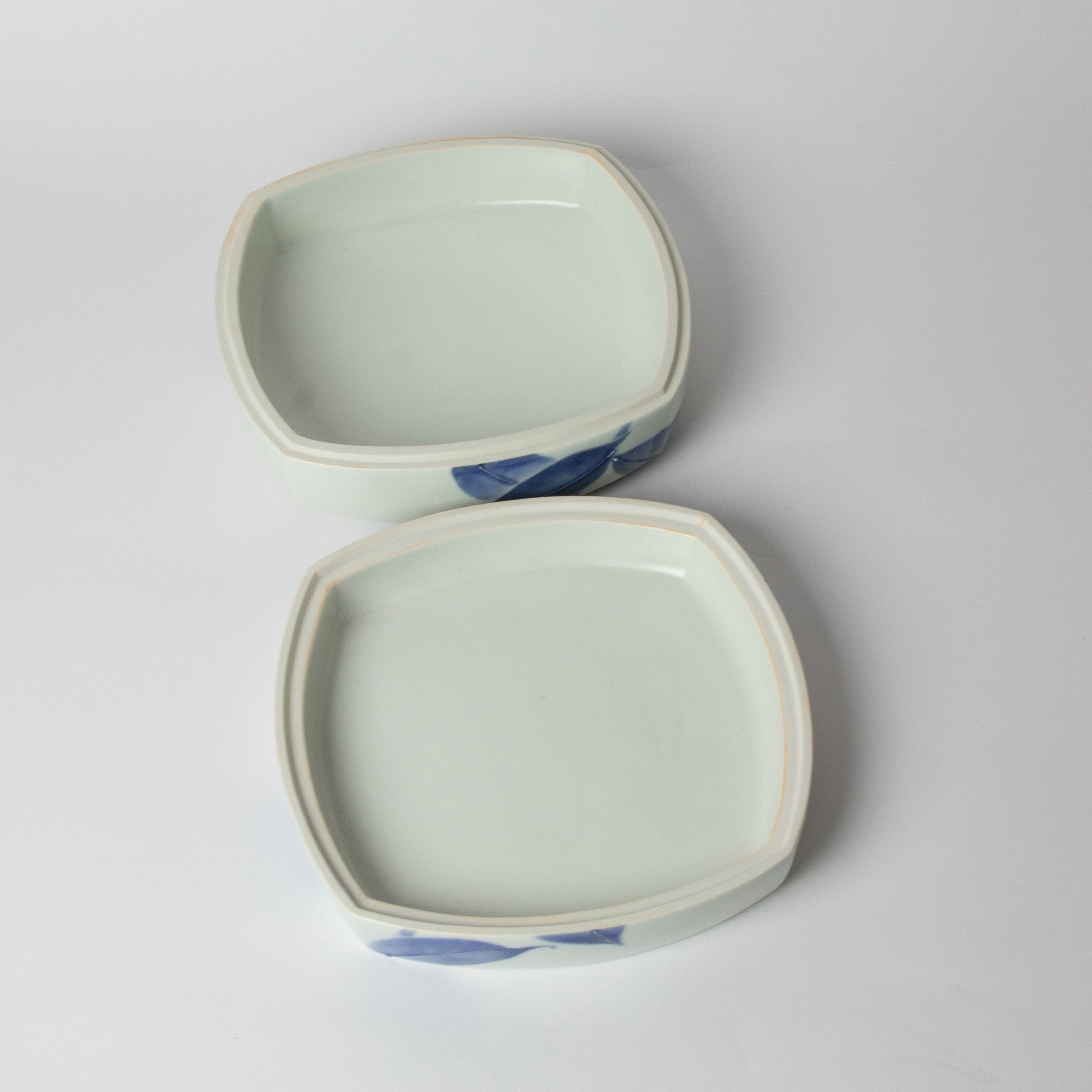 Vue de l'intérieur de la boîte en porcelaine japonaise ouverte, couvercle posé à côté. Œuvre de Tetsuya Ueda, au motif de camélia en bleu de cobalt.